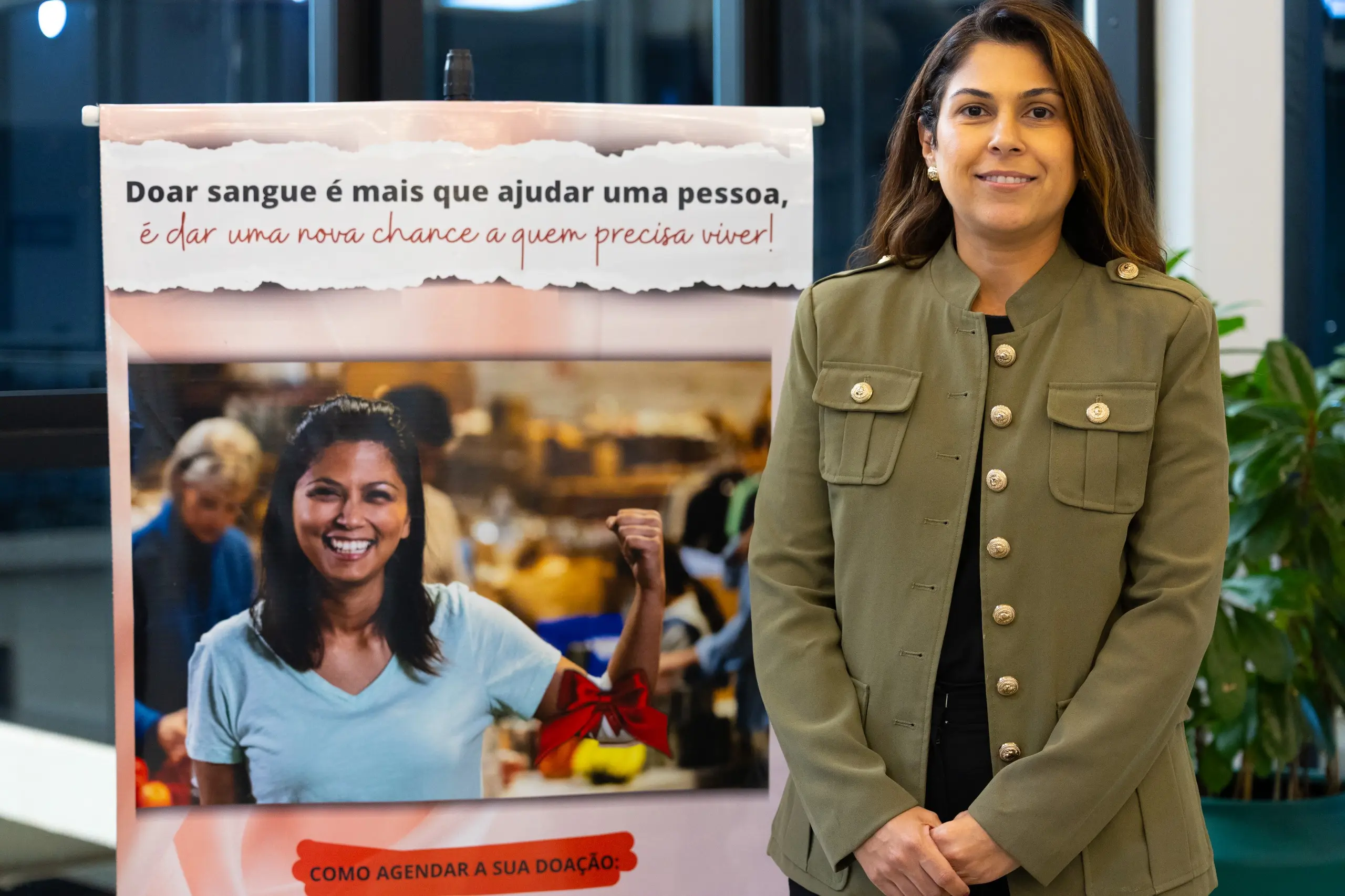 Gestora do Ambulatório do Fórum da Capital posa ao lado de banner da campanha de doação de sangue.