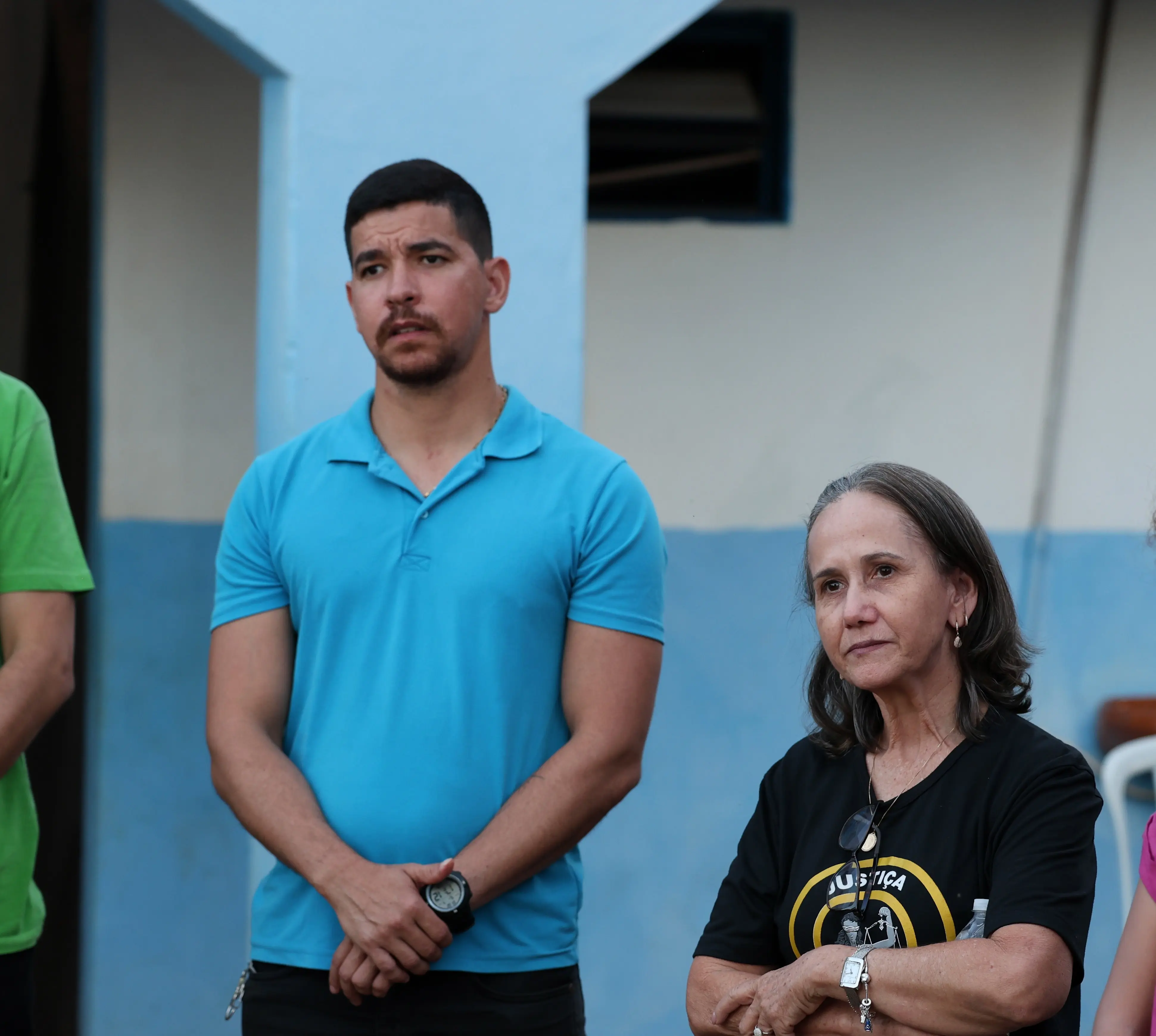 Foto quadrada que mostra o gerente de Almoxarifado da Prefeitura de Paranatinga, Rodrigo Maciel, em pé, em roda com outras pessoas em frente à escola onde ocorreu o mutirão Justiça em Ação. Ele é um homem branco, de cabelo, barba e olhos castanhos, usando calça preta e camiseta polo azul clara. 