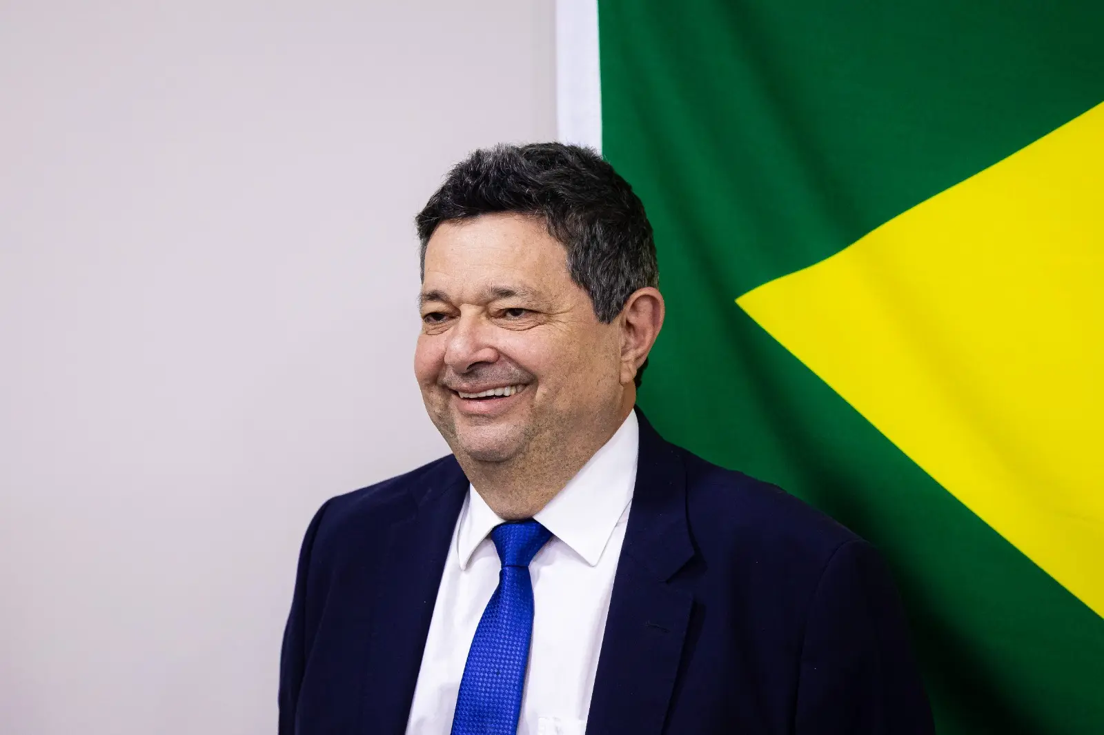 O corregedor, desembargador José Luiz Leite Lindote, aparece em pé e está sorrindo, ele veste terno escuro, camisa branca e gravata azul. Ao fundo, parte da bandeira do Brasil ocupa a parede.